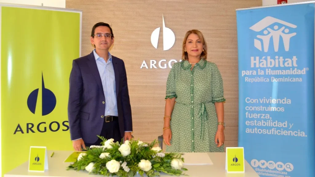 Un hombre y una mujer de pie entre el fondo lima de Argos y el fondo azul de Hábitat para la Humanidad