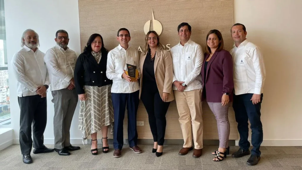 Ocho personas del equipo de Argos Dominicana posan con el galardón ante el panel de madera con el logo Argos