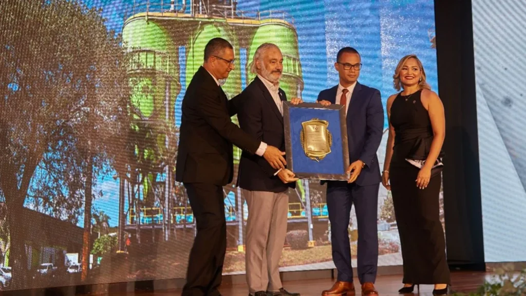 Entrega en escenario de una placa enmarcada a dos directivos de Argos, con los silos de la planta proyectados al fondo